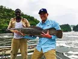A fisherman holding a large Vundu catfish while fishing in Murchison falls