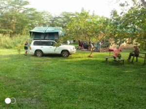 Guests relaxing around an evening campfire and outdoor seating area at Nguse River Camp, with the dark, dense Bugoma Forest illuminated by firelight