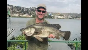An angler posing with a giant Nile perch on a fishing boat at sunset on Lake Victoria.